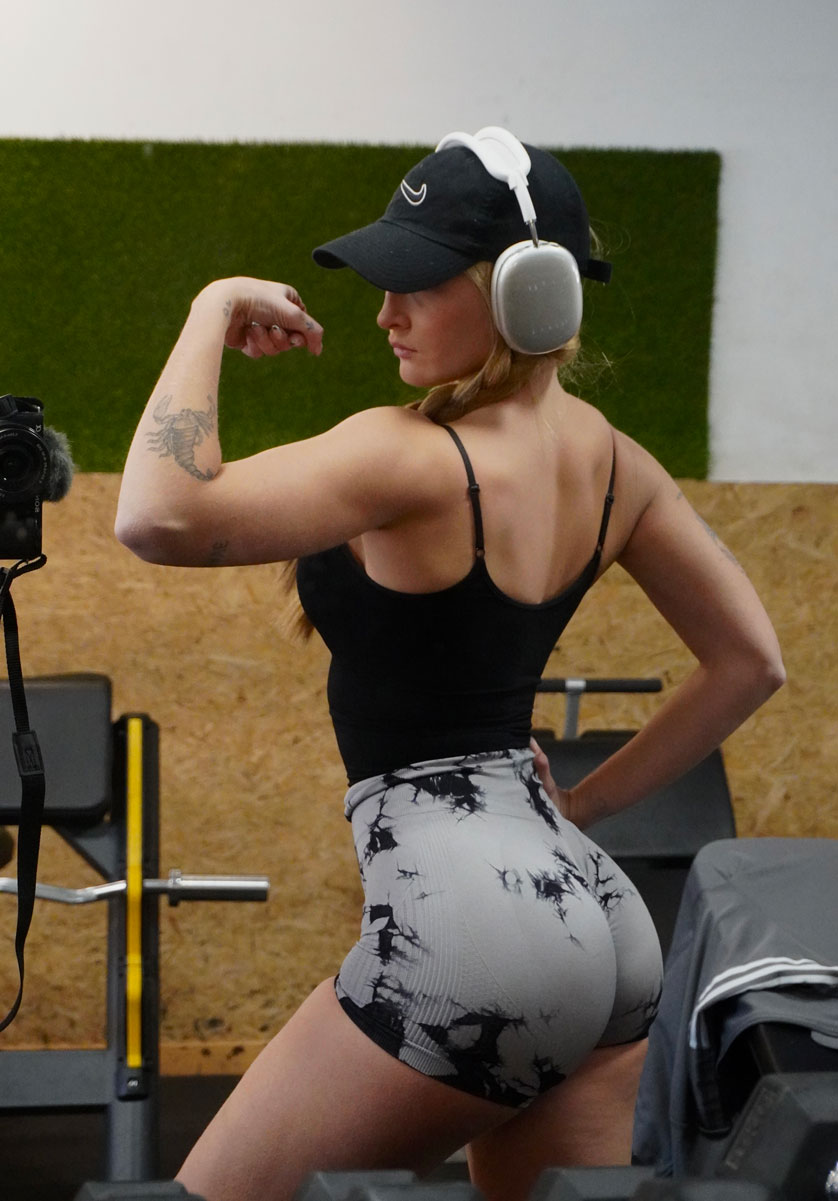 La entrenadora está flexionando la espalda y el brazo en el gimnasio.